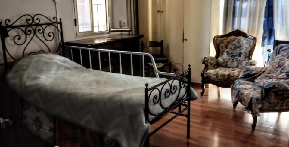 Camera della casa famiglia con letto in ferro battuto, poltrona in tessuto a fiori e pavimento in legno