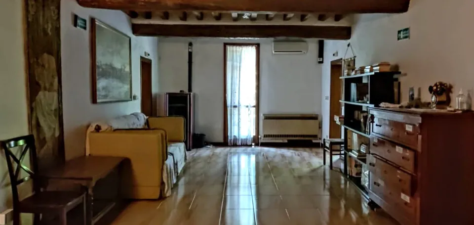 Il soggiorno della casa famiglia con travi in legno a vista, divano, libreria e cassettiera